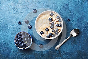 Bowl of oatmeal porridge with banana and blueberry on vintage table top view in flat lay style. Hot breakfast and homemade food. photo