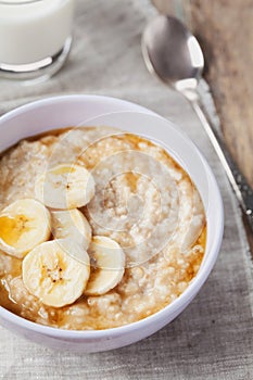 Bowl of oatmeal porridge with banana and caramel sauce on rustic table, hot and healthy breakfast