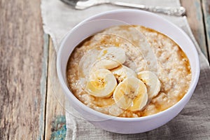 Bowl of oatmeal porridge with banana and caramel sauce on rustic table, hot and healthy breakfast