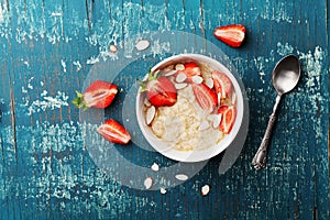 Bowl of oatmeal porridge with strawberry and almond flakes on vintage teal table top view in flat lay style. Healthy breakfast.