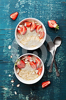 Bowl of oatmeal porridge with strawberry and almond flakes on wooden teal table top view in flat lay style. Healthy breakfast.