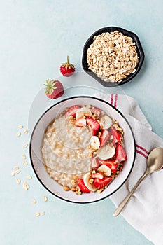 Bowl of oatmeal porridge with strawberry and banana on blue table top view. Healthy and diet breakfast