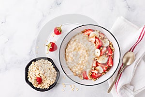 Bowl of oatmeal porridge with strawberry and banana on white table top view. Healthy and diet breakfast