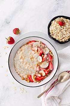 Bowl of oatmeal porridge with strawberry and banana on white table top view. Healthy and diet breakfast