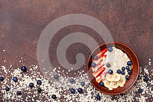 Bowl of oatmeal porridge with strawberry, blueberry and banana on brown table top view. Healthy breakfast