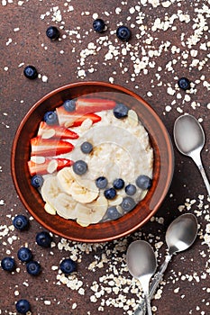 Bowl of oatmeal porridge with strawberry, blueberry and banana on kitchen table top view. Healthy breakfast