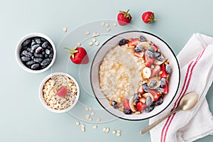 Bowl of oatmeal porridge with various berry and banana on blue table top view. Healthy and diet breakfast