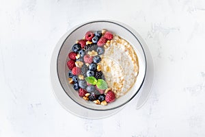 Bowl of oatmeal porridge with various berry and nuts on white table top view. Healthy and diet breakfast