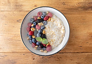 Bowl of oatmeal porridge with various berry and nuts on wooden table top view. Healthy and diet breakfast