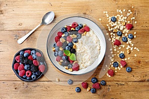 Bowl of oatmeal porridge with various berry on wooden table top view. Healthy and diet breakfast