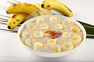 Bowl of oats porridge with bananas on white background.