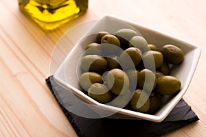 A bowl of olives with the olive oil bottle in the background