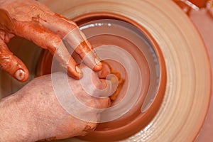 A bowl of orange clay rotates on a potter`s wheel