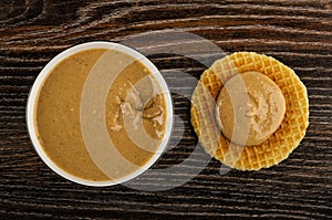 Bowl with peanut paste, sandwich with peanut butter on table. Top view