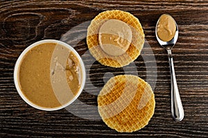 Bowl with peanut paste, sandwich with peanut butter, wafer, spoon with peanut paste on wooden table. Top view