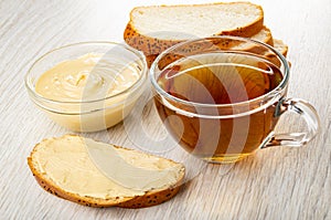 Bowl with peanut paste, slices of bun with poppy, sandwich with peanut butter, cup of tea on table