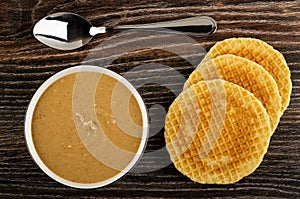 Bowl with peanut paste, spoon, round wafers on wooden table. Top view