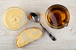 Bowl with peanut paste, spoon, sandwich with peanut butter, cup of tea on table. Top view