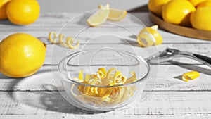 Bowl with peel pieces, fresh lemons and zester on white wooden table