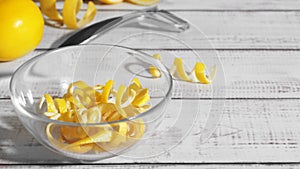 Bowl with peel pieces, fresh lemons and zester on white wooden table. Space for text