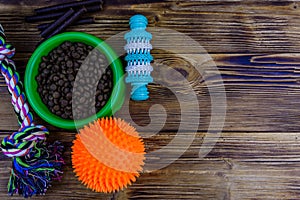 Bowl with pet food, dog toy for teeth cleaning, rope with tied knots and toy ball on a wooden background. Top view