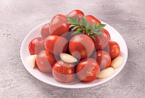 A bowl with pickled tomatoes and spices on a gray background