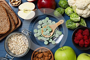 Bowl with pills and foodstuff on blue wooden table, flat lay. Prebiotic supplements