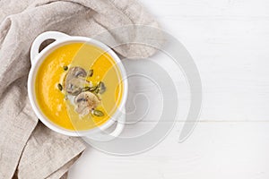 Bowl of Pumpkin and Mushrooms Soup with Cream and Pumpkin Seeds on Linen Napkin White Wooden Background Top View Copy Space