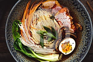 Bowl of ramen soup with pork, shiitake and enoki mushrooms, marinated egg and vegetables, close up.