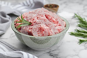 Bowl of raw fresh minced meat with rosemary on white marble tabl