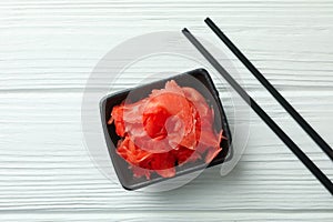 Bowl with red pickled ginger and chopsticks on white wooden background