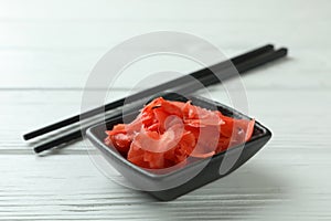 Bowl with red pickled ginger and chopsticks on white wooden background