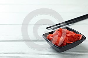 Bowl with red pickled ginger and chopsticks on white wooden background