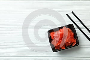 Bowl with red pickled ginger and chopsticks on white wooden background