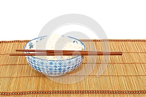 Bowl of rice with chopsticks and table mat against white backgro