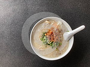 A bowl of rice congee with minced pork, boiled egg topped with fried shallot and fresh coriander