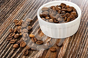 Bowl with roasted coffee beans, scattered coffee beans on wooden table