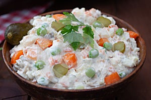 Bowl of russian salad olivier with meat and vegetables on a wooden table