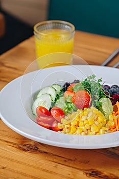 A bowl of salad with a glass of orange juice on a wooden table