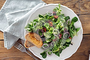 Bowl salad green mache leaves baked tomatoes on wooden table