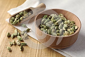 Bowl and scoop of dry cardamom pods on wooden table