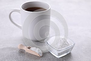 Bowl and scoop of sweet fructose powder near cup with tea on light grey table