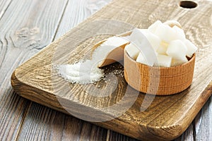 Bowl and scoop with white sand and lump sugar on wooden background