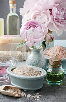 Bowl of sea salt, glass bottle of essential oil and peonies in t