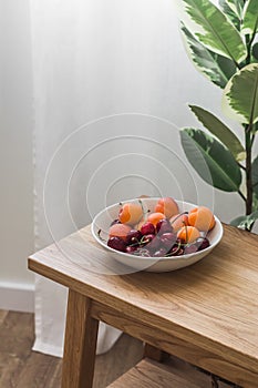 A bowl with seasonal summer fruits and berries on a wooden oak bench in a cozy living room