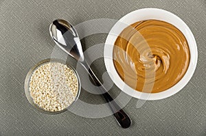 Bowl with sesame seeds, spoon, white bowl with peanut butter on table. Top view