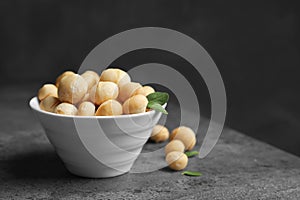 Bowl with shelled organic Macadamia nuts on table against dark background.