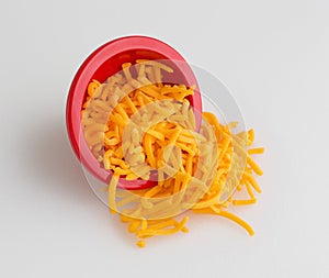 Bowl of shredded sharp cheddar cheese spilling on cutting board