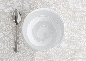 Bowl and silver spoon empty on patterned table cloth - Top view