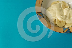 Bowl of sliced banana and yoghurt in a bowl on bright blue background - minimal, copy space